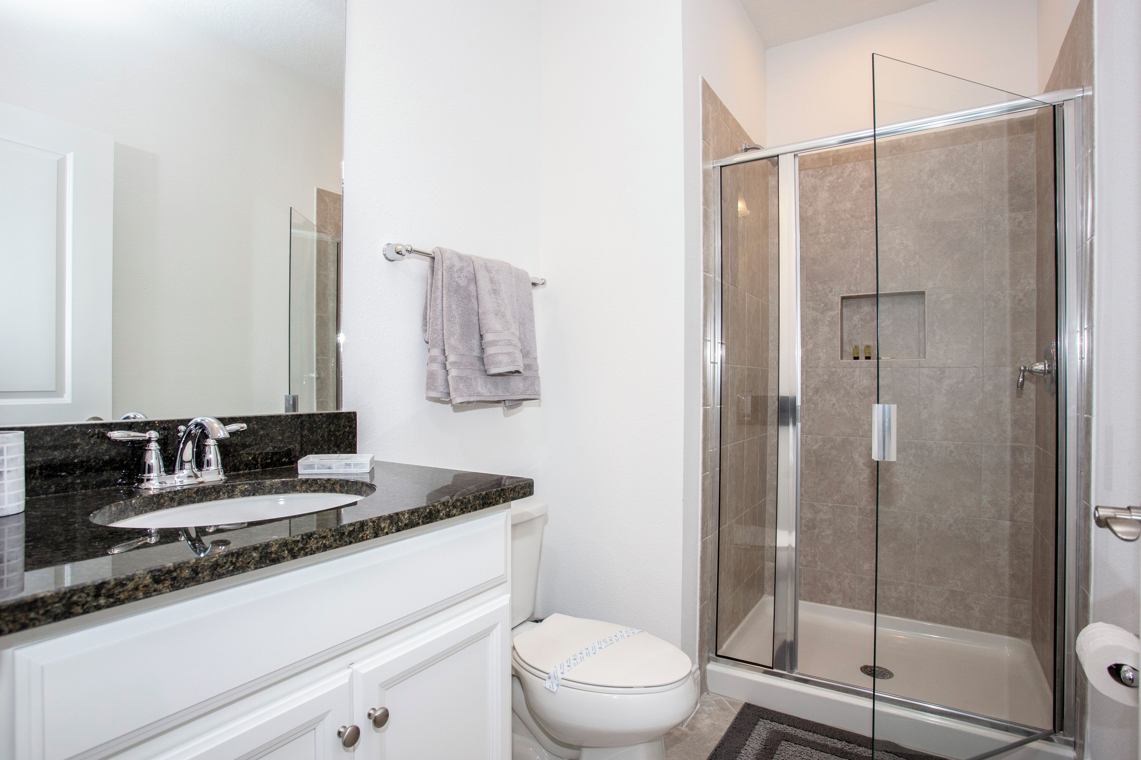 Un baño moderno con ducha de vidrio, inodoro blanco y lavamanos de granito.