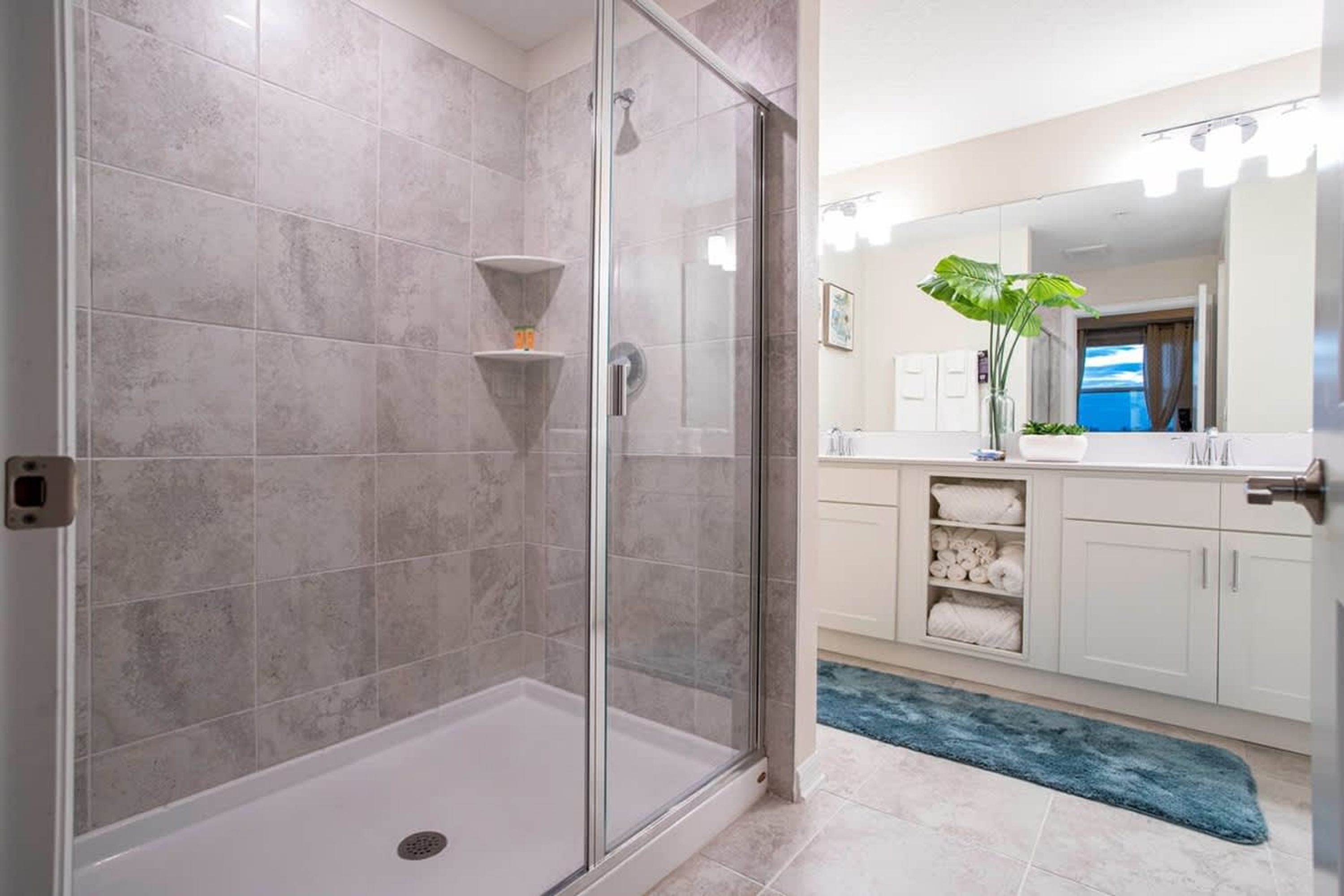 Une salle de bain avec une douche à parois de verre, des murs carrelés, un lavabo et un miroir.