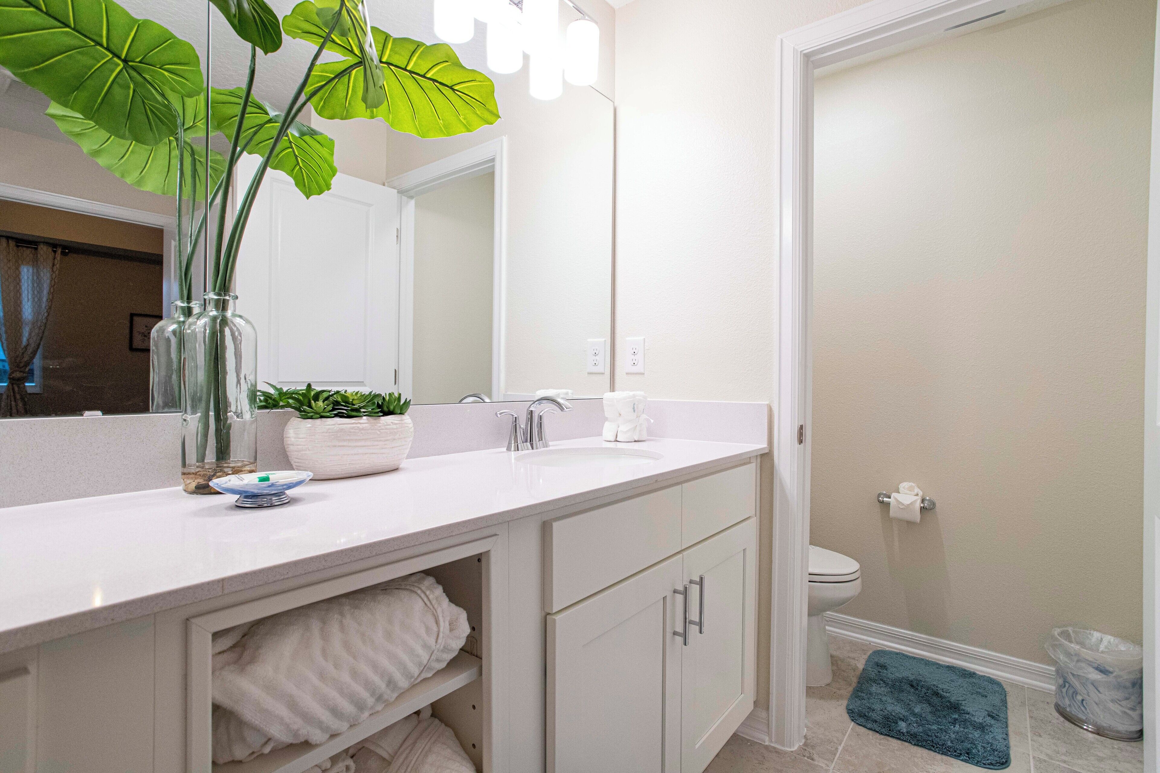 A modern bathroom with a white vanity, a large mirror, and a potted plant.