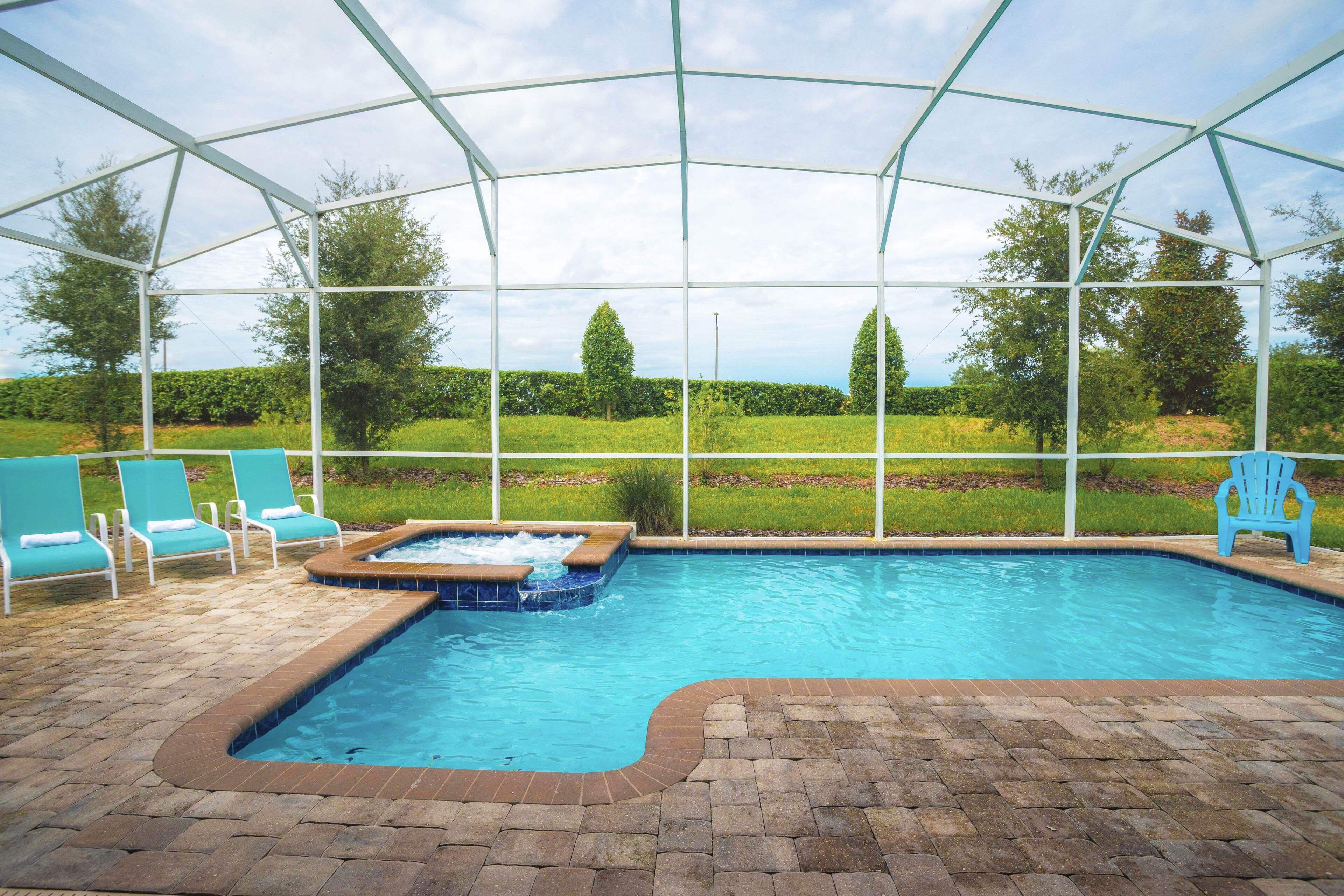 A covered swimming pool with a hot tub, surrounded by lounge chairs and a brick patio.