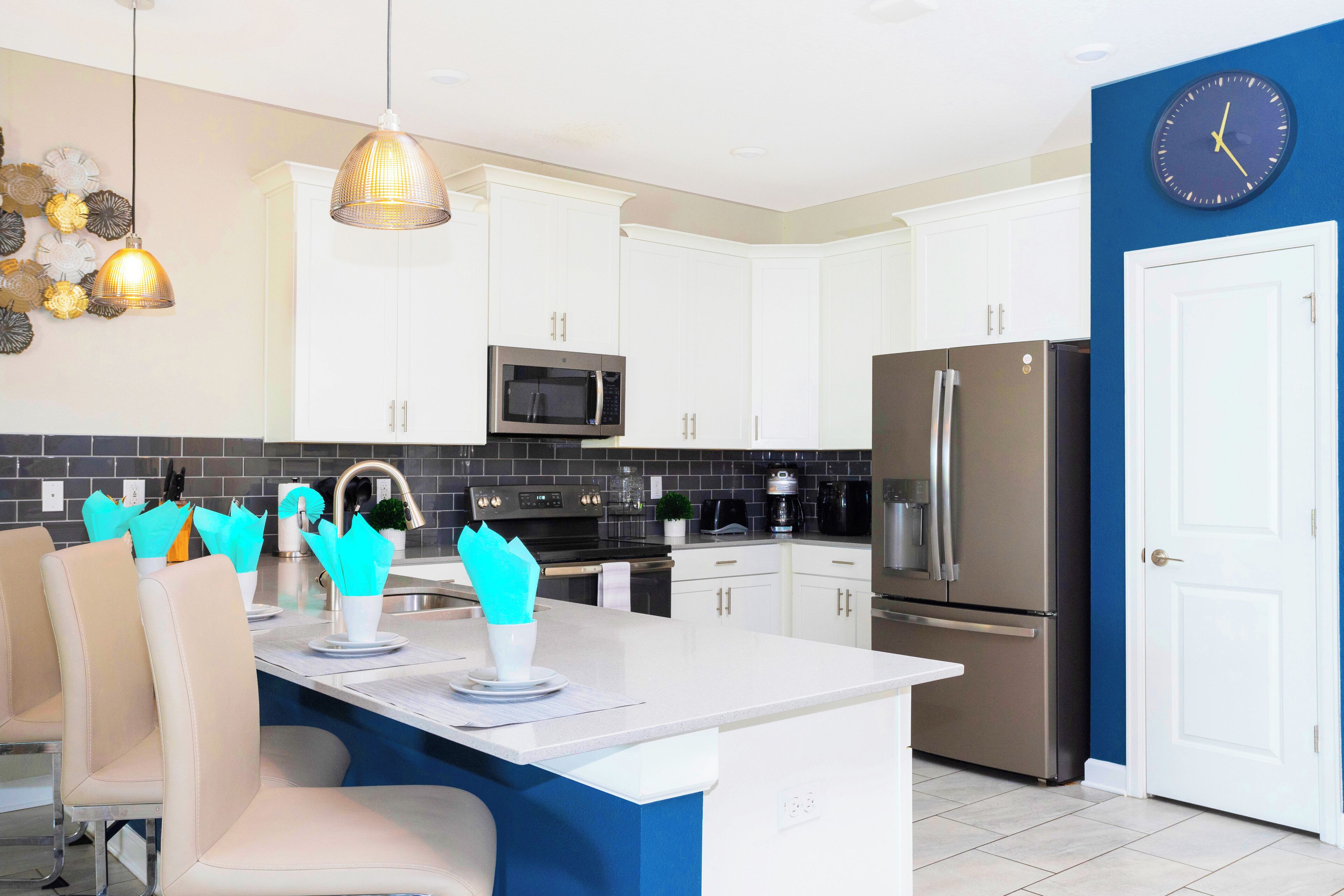 A modern kitchen with white cabinets, a stainless steel refrigerator, a microwave, and a clock on the wall.