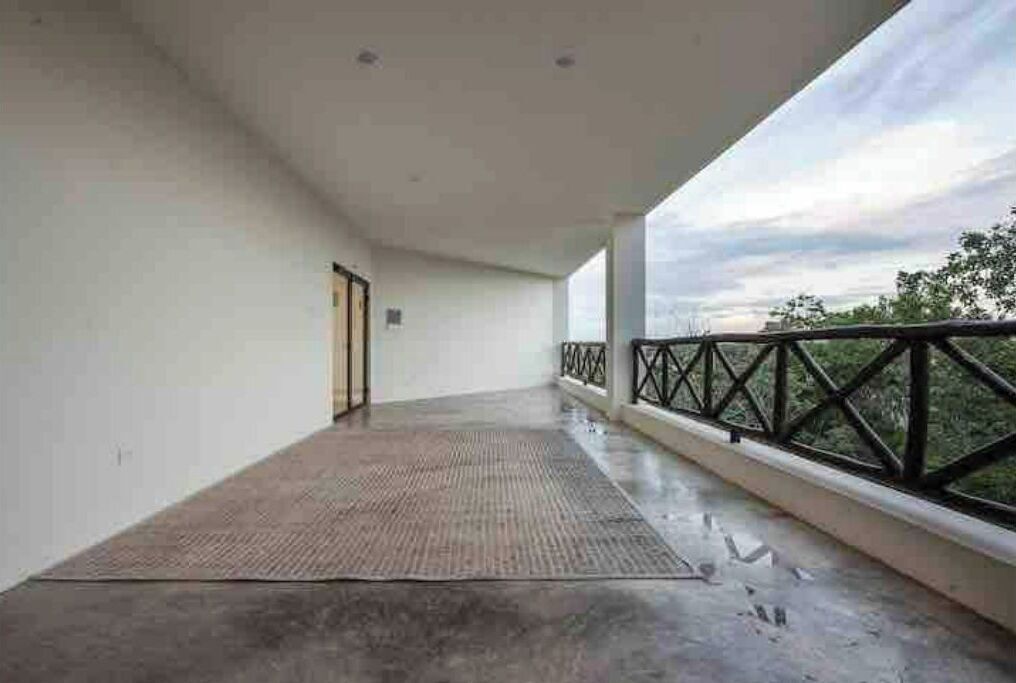 Ein Balkon mit Betonboden und Metallgeländer, der auf eine grüne Landschaft blickt.
