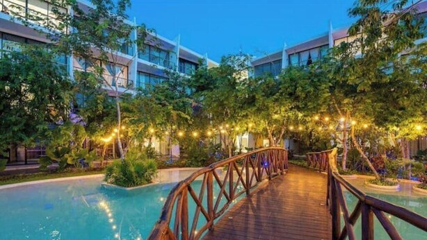 A wooden bridge over a pool with surrounding trees and buildings. - Luxurious Apartment With Jacuzzi Privado (Tulum)