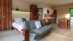 A modern bedroom with a bed, a grey sofa, wooden cabinets, and a kitchenette. - Luxurious Apartment With Jacuzzi Privado (Tulum)