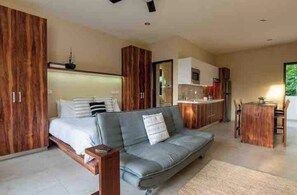Ein modernes Schlafzimmer mit einem Bett, einem grauen Sofa, Holzschränken und einer Küchenzeile.
