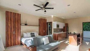 A modern bedroom with a bed, a wooden wardrobe, a grey sofa, and a ceiling fan. - Luxurious Apartment With Jacuzzi Privado (Tulum)
