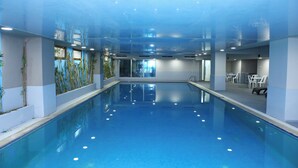 An indoor swimming pool with clear water, surrounded by walls with windows and indoor plants. - Deluxe Hotel Ganja (Ganja)