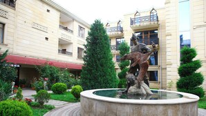 A courtyard with a central fountain, surrounded by well-maintained greenery and a building with balconies. - Deluxe Hotel Ganja (Ganja)