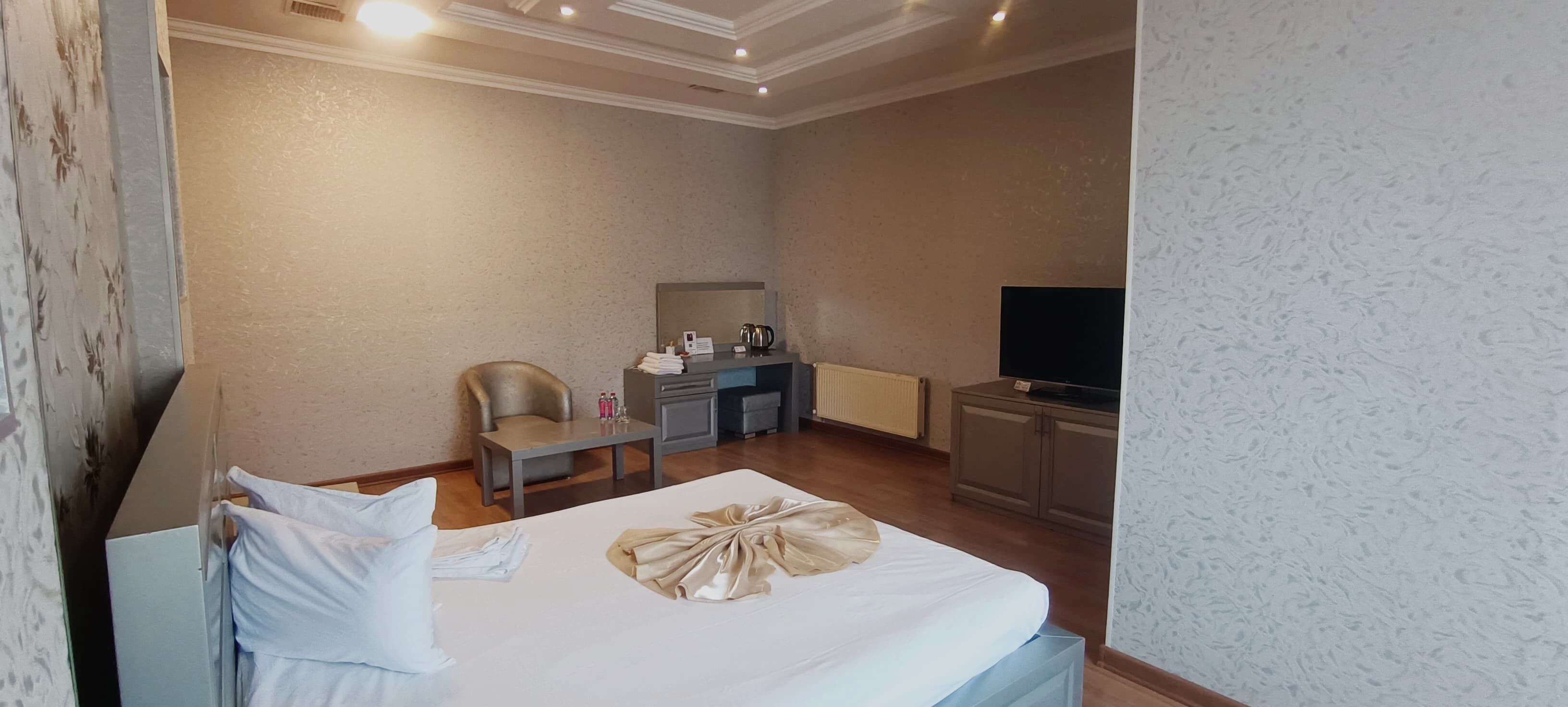 A hotel room with a bed, a desk, a chair, a television, and a radiator.
