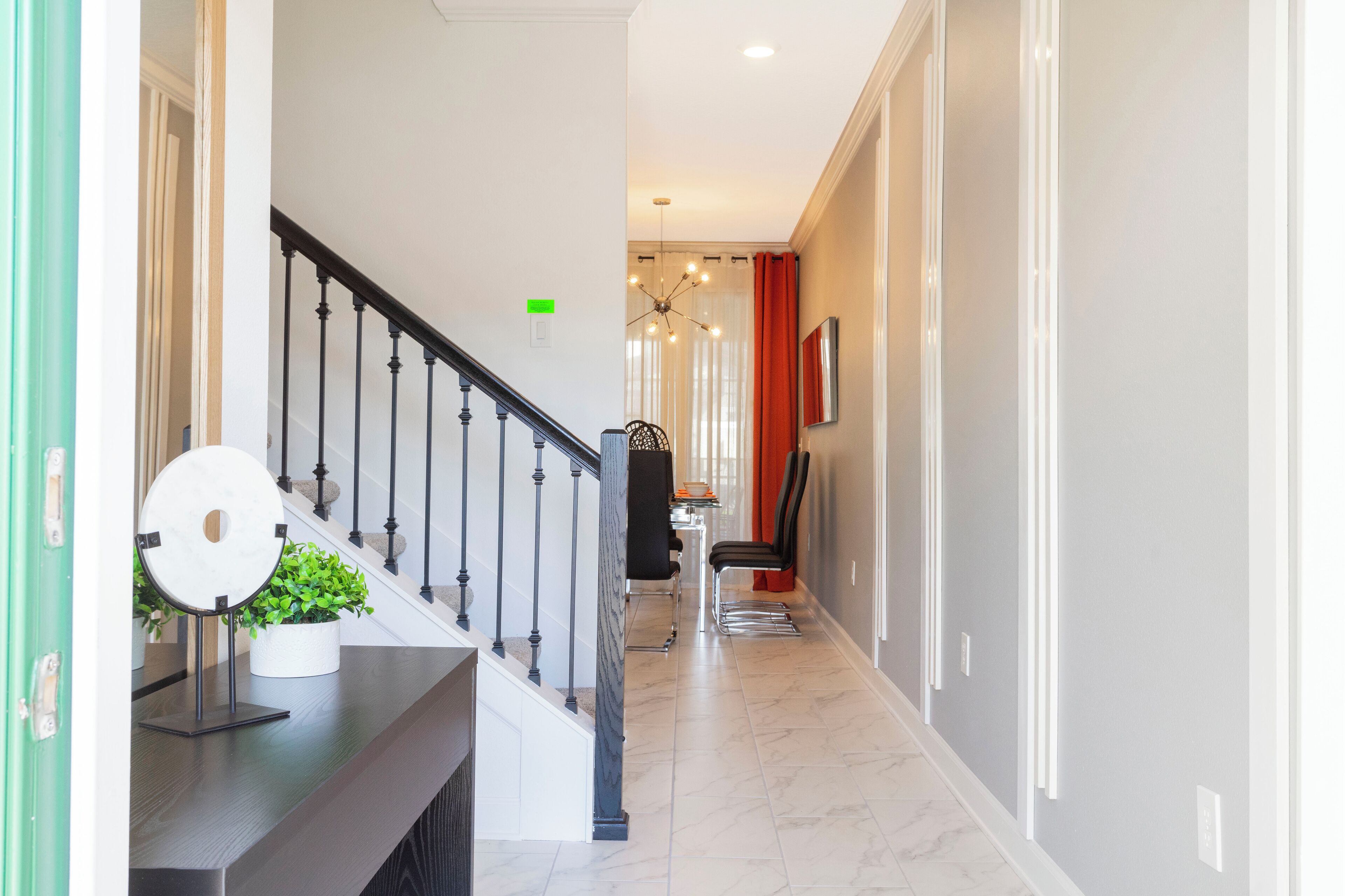 A modern hallway with a staircase, a potted plant, a dining area, and a red curtain.