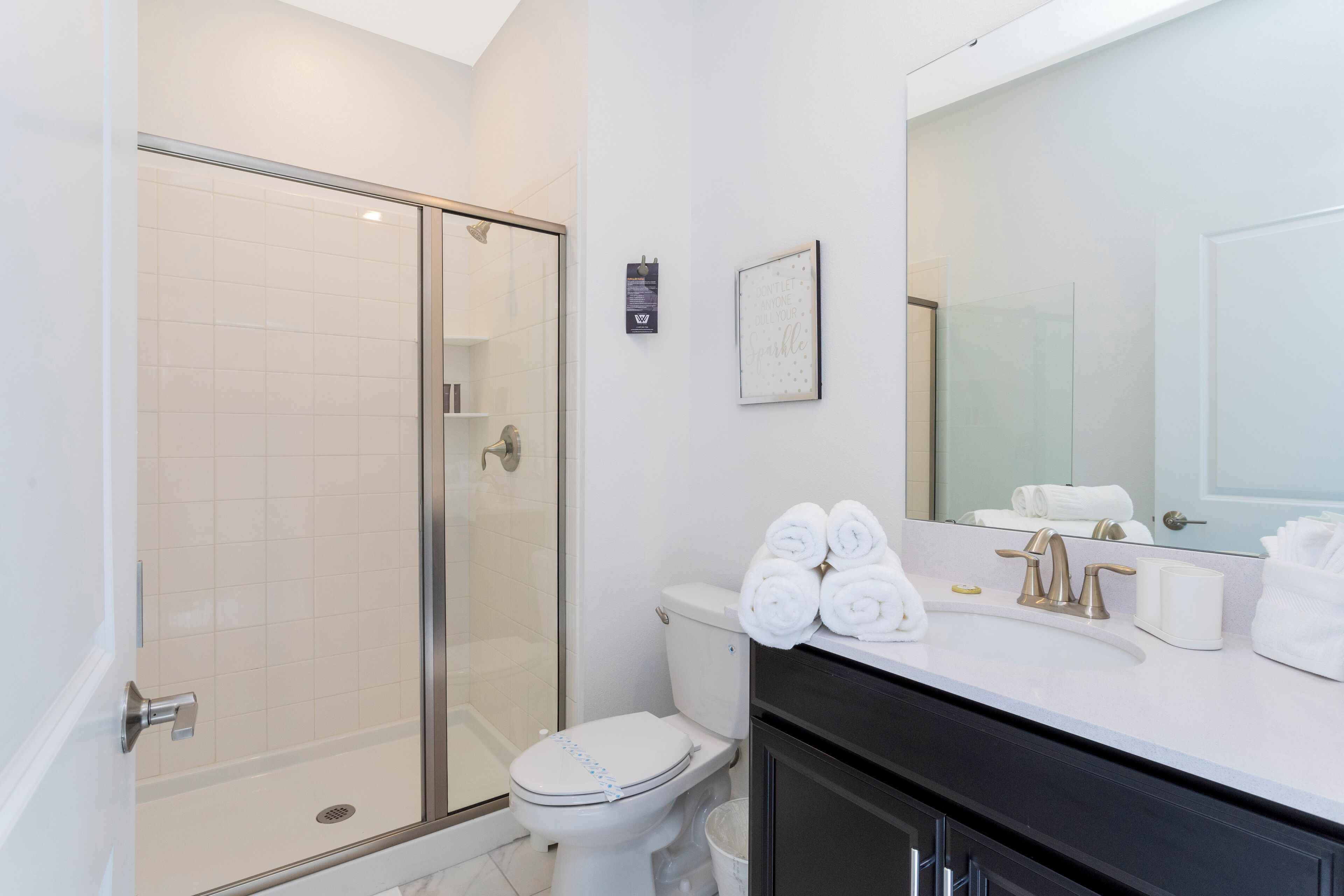 Un bagno moderno con doccia vetro, un water e un lavandino con asciugamani.