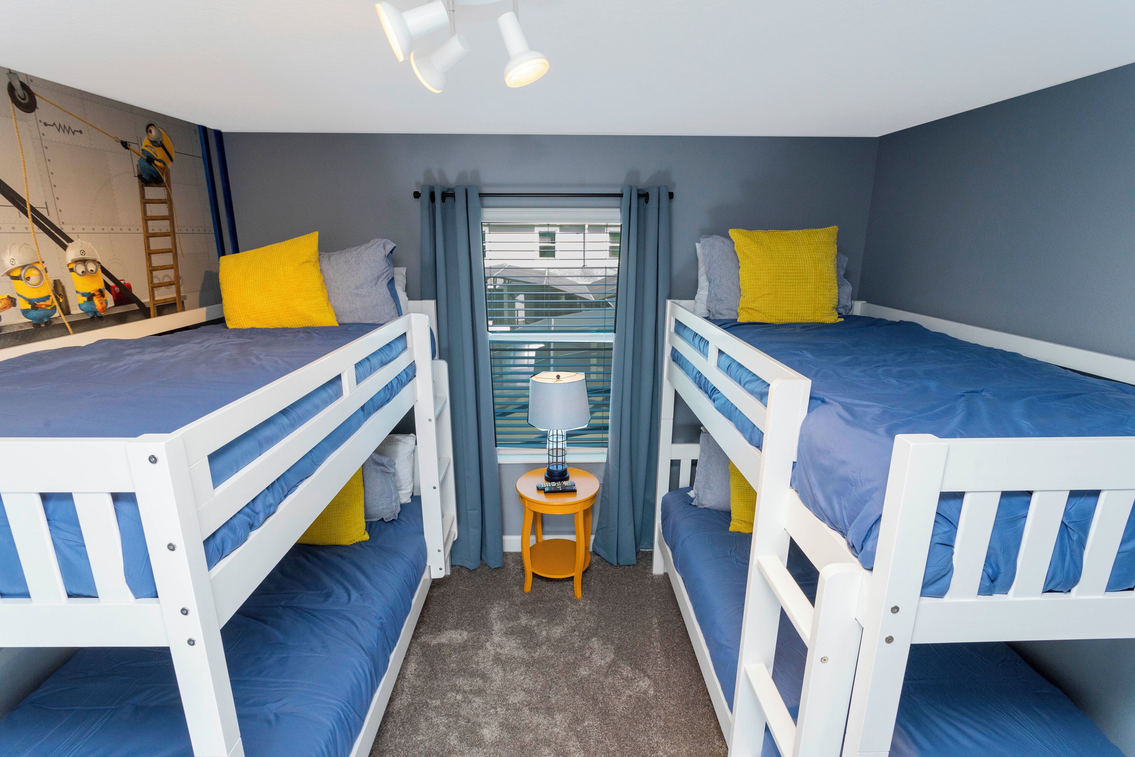 A room with two bunk beds, a small table with a lamp, and a window with curtains.