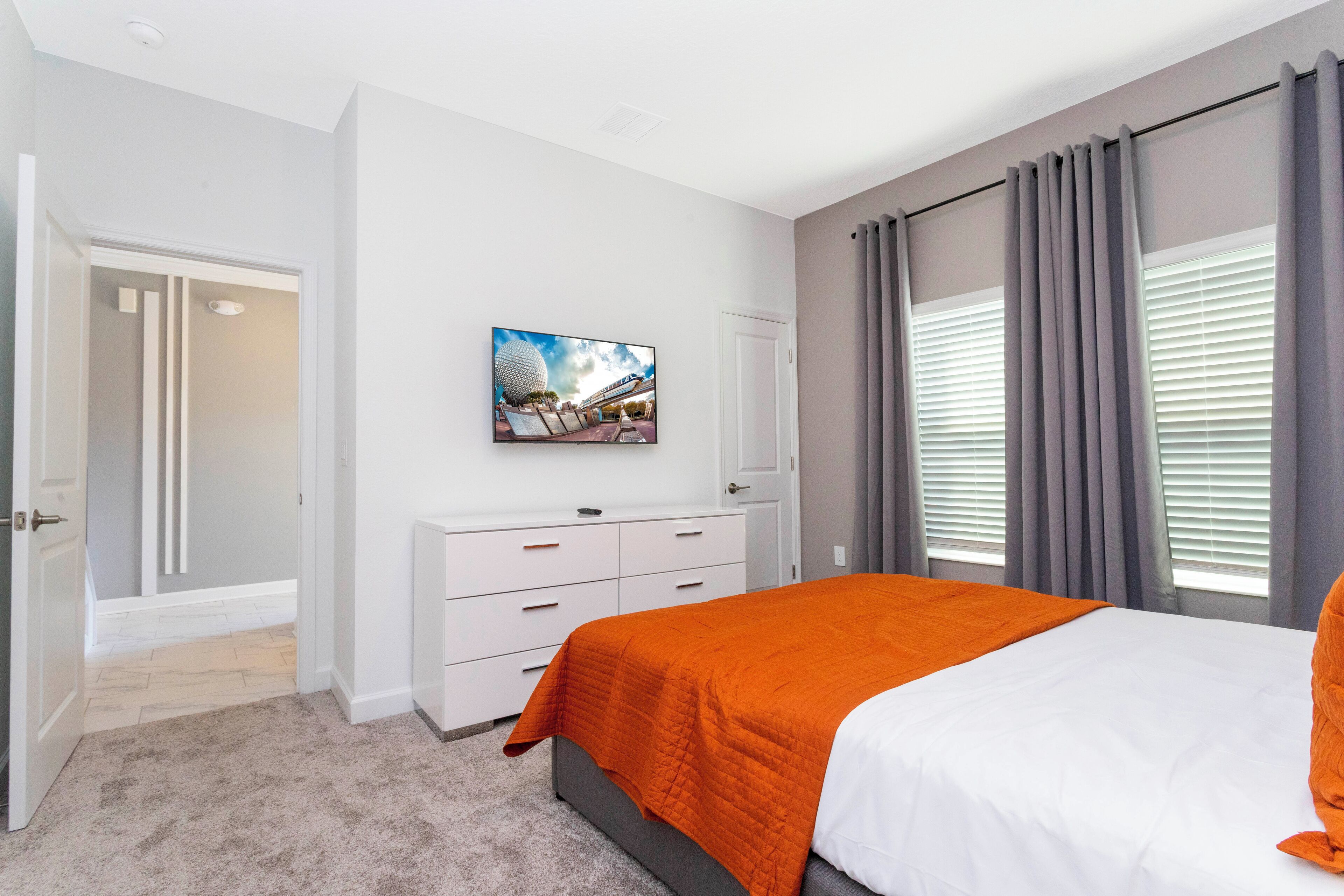 Un dormitorio con cama, televisor en la pared, armario y puerta que da a otra habitación.