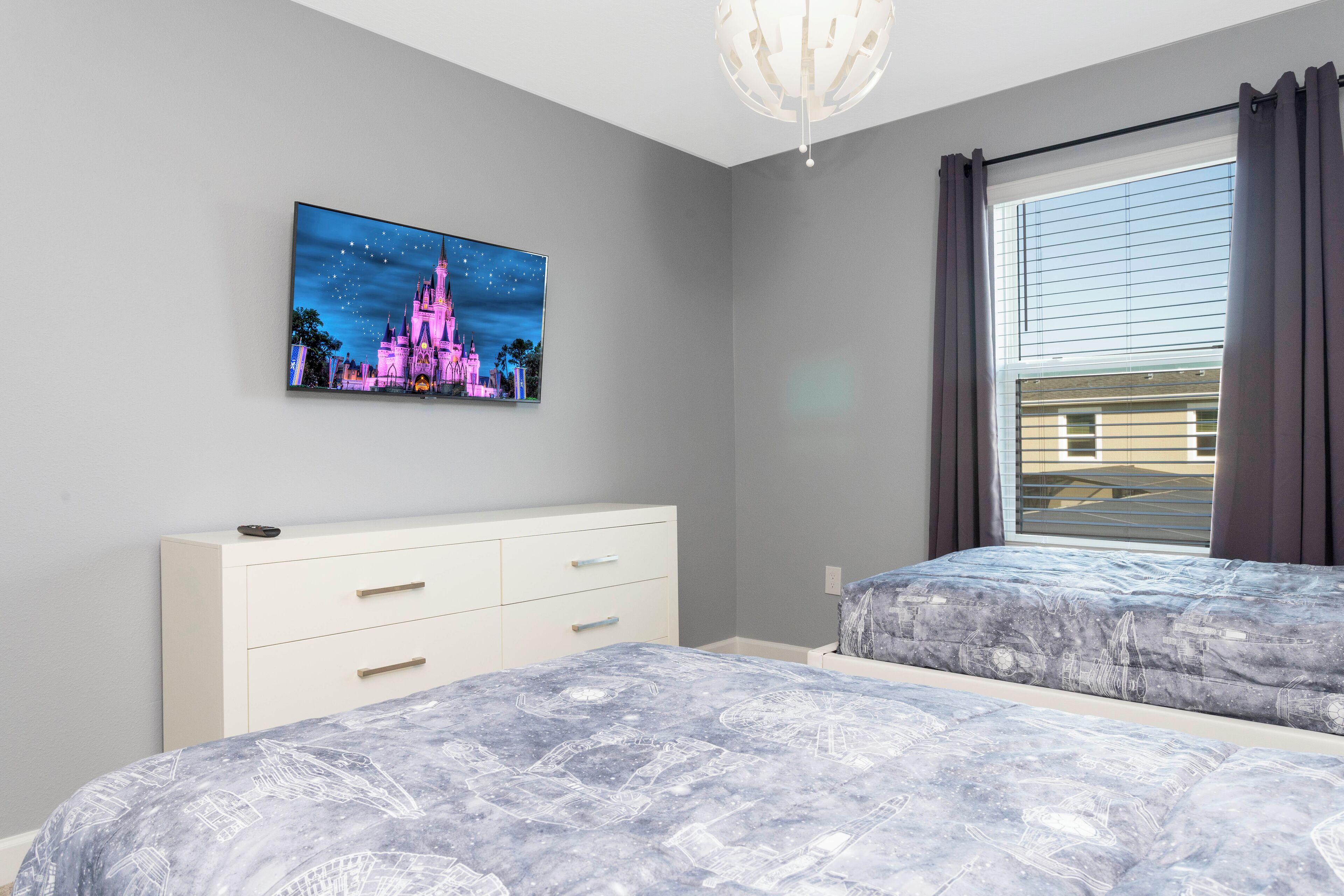 A bedroom with a bed, a dresser, a window with curtains, and a wall-mounted picture of a castle.