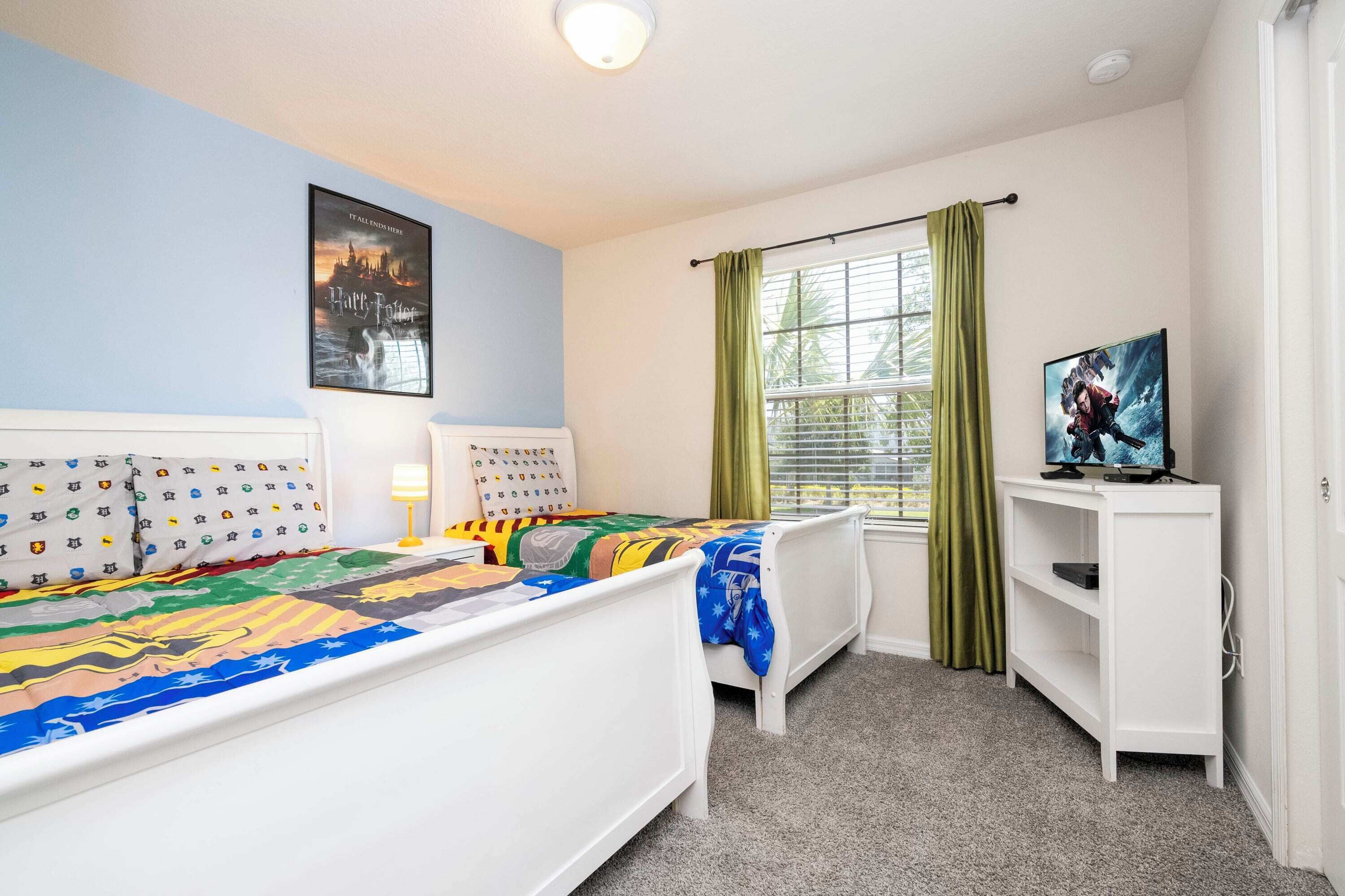 Une chambre avec deux lits, une fenêtre avec des rideaux, un tableau accroché au mur et un téléviseur posé sur un meuble.