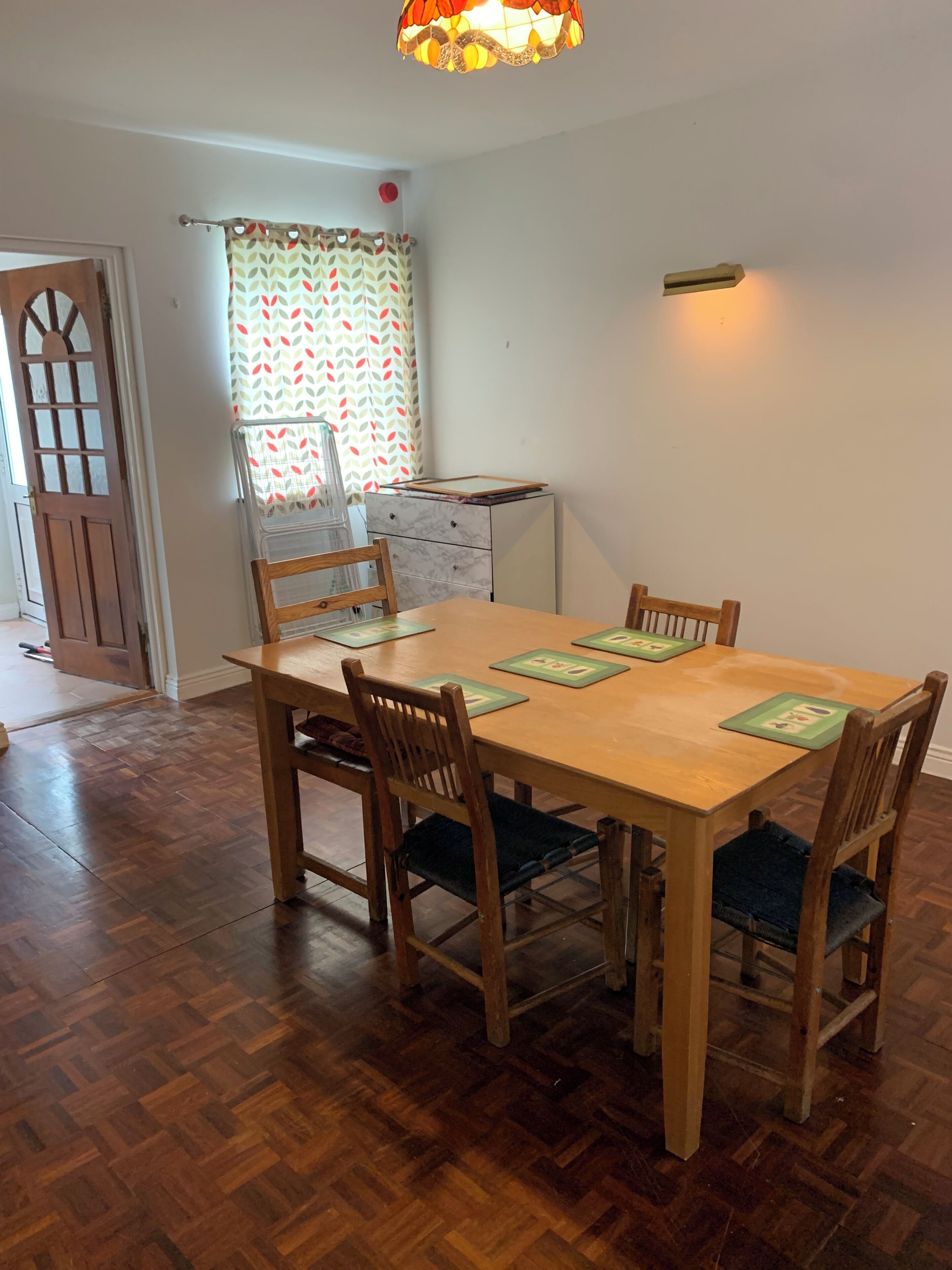 A dining area with a wooden table and chairs, a patterned curtain, a small cabinet, and a door with a window.