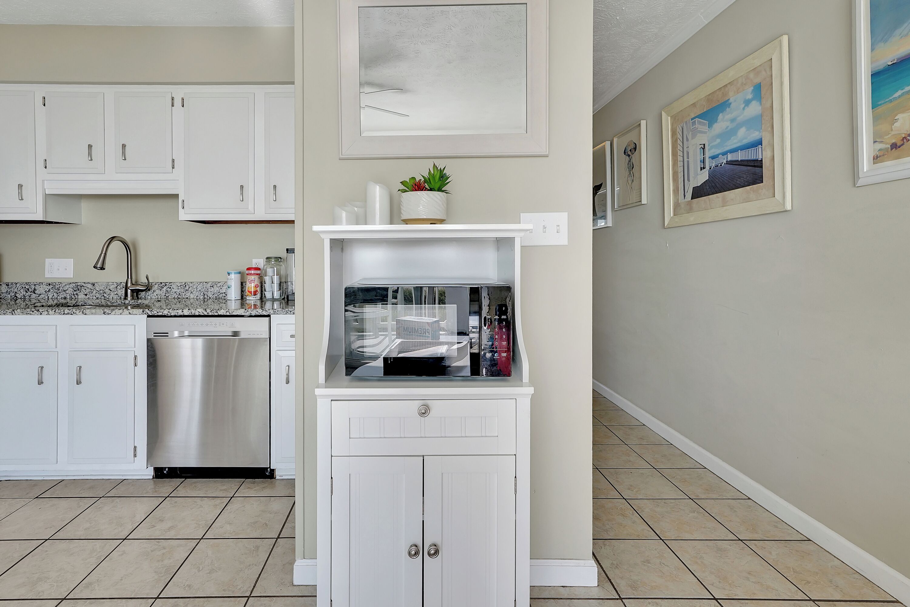 A kitchen with white cabinets, a dishwasher, a countertop with a sink, and a shelf with a potted plant.