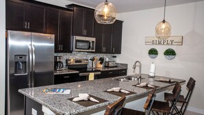 A modern kitchen with dark cabinets, stainless steel appliances, a granite countertop, and a central island with bar stools. - Four Bedroom Storey Lake Resort Close to Disney w Pool 3063 (Kissimmee)