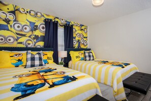A hotel room with two beds, each covered with a Minions-themed duvet. There is a window with curtains, a bedside table with a lamp, and a small stool. - Four Bedroom Storey Lake Resort Close to Disney w Pool 3063 (Kissimmee)