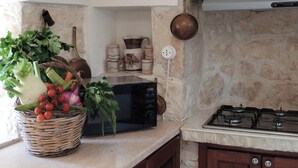 Una cocina con microondas, una cesta de verduras frescas, una estufa a gas y una pared de piedra.