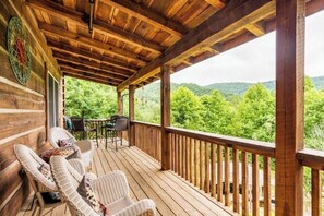 Une terrasse en bois, dotée de chaises et d’une table en osier, qui offre une vue sur un paysage boisé.