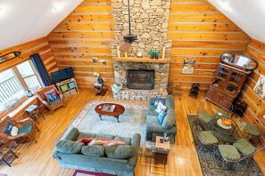 Un acogedor interior de cabaña de madera con chimenea de piedra, paredes de madera, un sofá y un comedor.