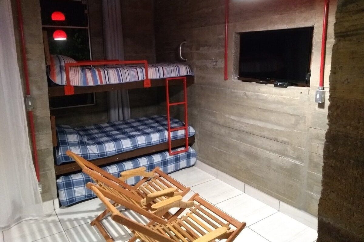 Une petite chambre avec des lits superposés, une télévision et une chaise en bois.