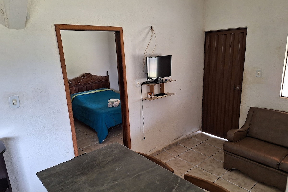 Une petite pièce, de taille modeste, comprenant un lit, un téléviseur fixé au mur, un canapé marron et une petite table.
