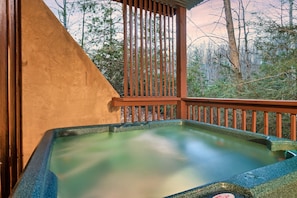 Relax in a hot tub on a serene outdoor deck surrounded by lush greenery.