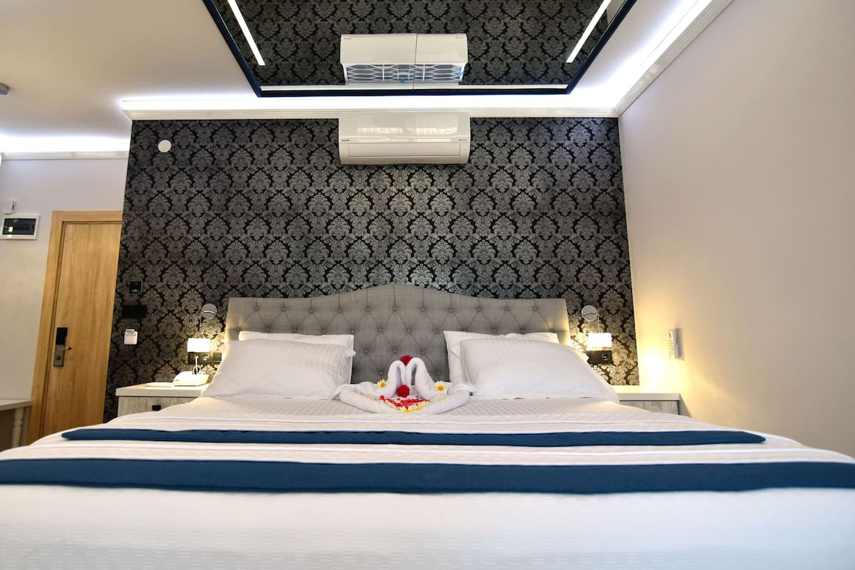 Una habitación de hotel con una cama grande, dos mesitas de noche, una lámpara en el techo y un aire acondicionado instalado en la pared.
