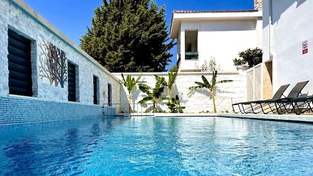A swimming pool with clear blue water, surrounded by a white building with a tiled exterior and a balcony with sun loungers. - Tahir Ağa Hotel Datça (Datça)