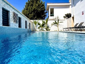A swimming pool with clear blue water, surrounded by a white building with a tiled exterior and a balcony with sun loungers. - Tahir Ağa Hotel Datça (Datça)