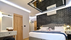 A modern bedroom with a large bed, a vanity with a mirror, and a wall-mounted air conditioner. - Tahir Ağa Hotel Datça (Datça)