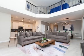 Een ruime woonkamer met twee banken, een salontafel en een trap naar een balkon.