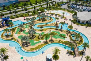 Luchtbeeld van een resort met een groot zwembad, palmbomen en een glijbaan.