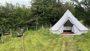 A tent with a simple, open design, surrounded by a grassy area with a few chairs and a barbecue grill. - Double Bell Tent Farm Stay (Loughborough)