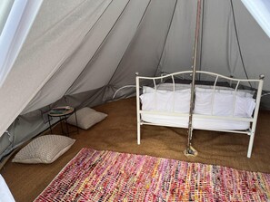 A tent with a bed, pillows, a small table, and a colorful rug. - Double Bell Tent Farm Stay (Loughborough)