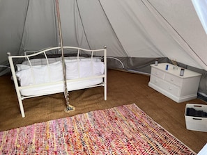 A tented room with a bed, a dresser, and a colorful rug. - Double Bell Tent Farm Stay (Loughborough)