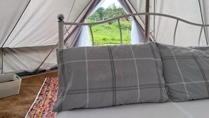 A bed in a tent with a view of a green field. - Double Bell Tent Farm Stay (Loughborough)
