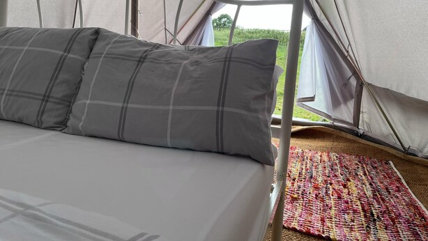 A bed with grey plaid bedding inside a tent. - Double Bell Tent Farm Stay (Loughborough)