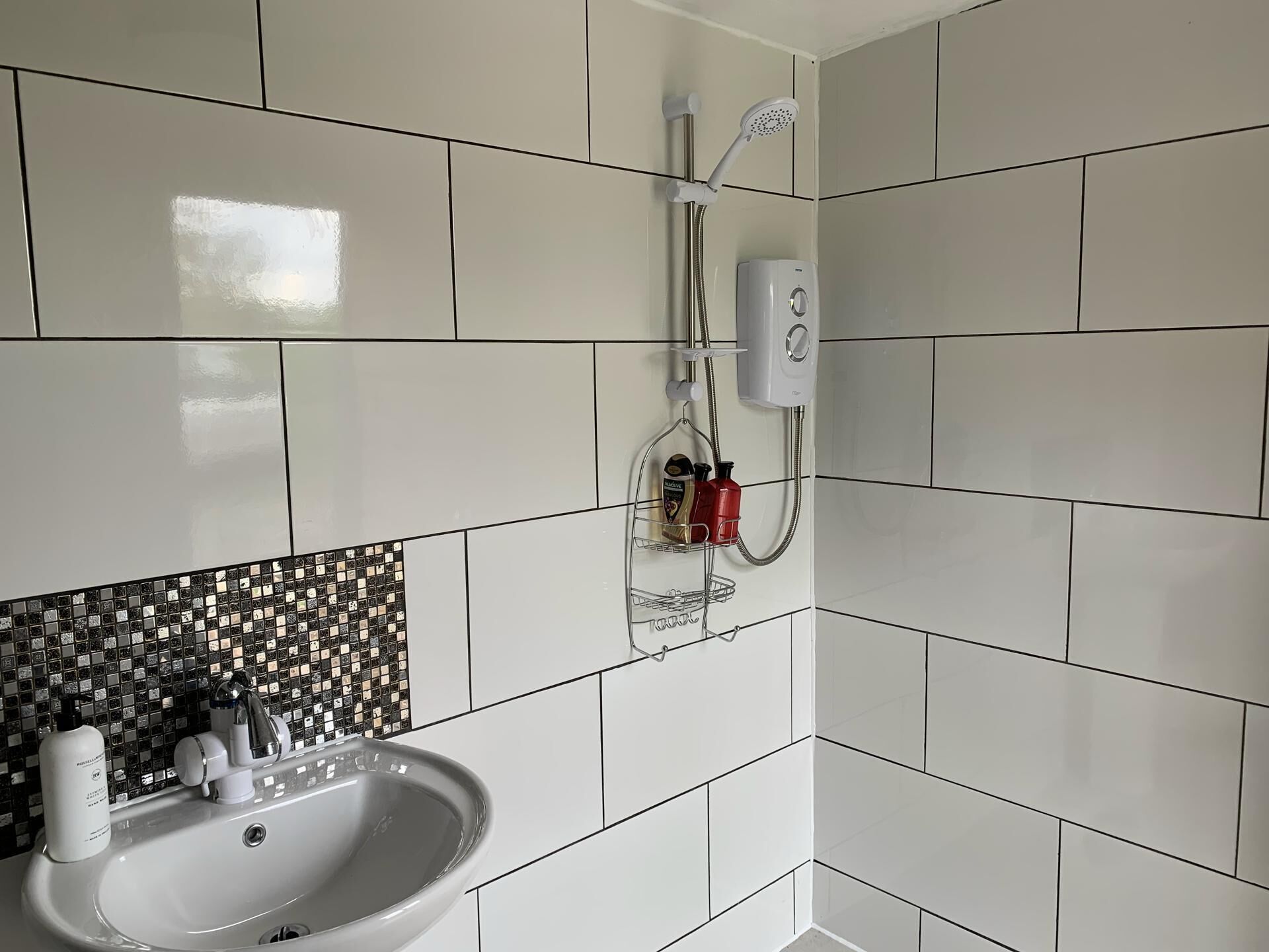 Une salle de bain avec des carreaux blancs, un lavabo en verre, une douche et un distributeur de savon.