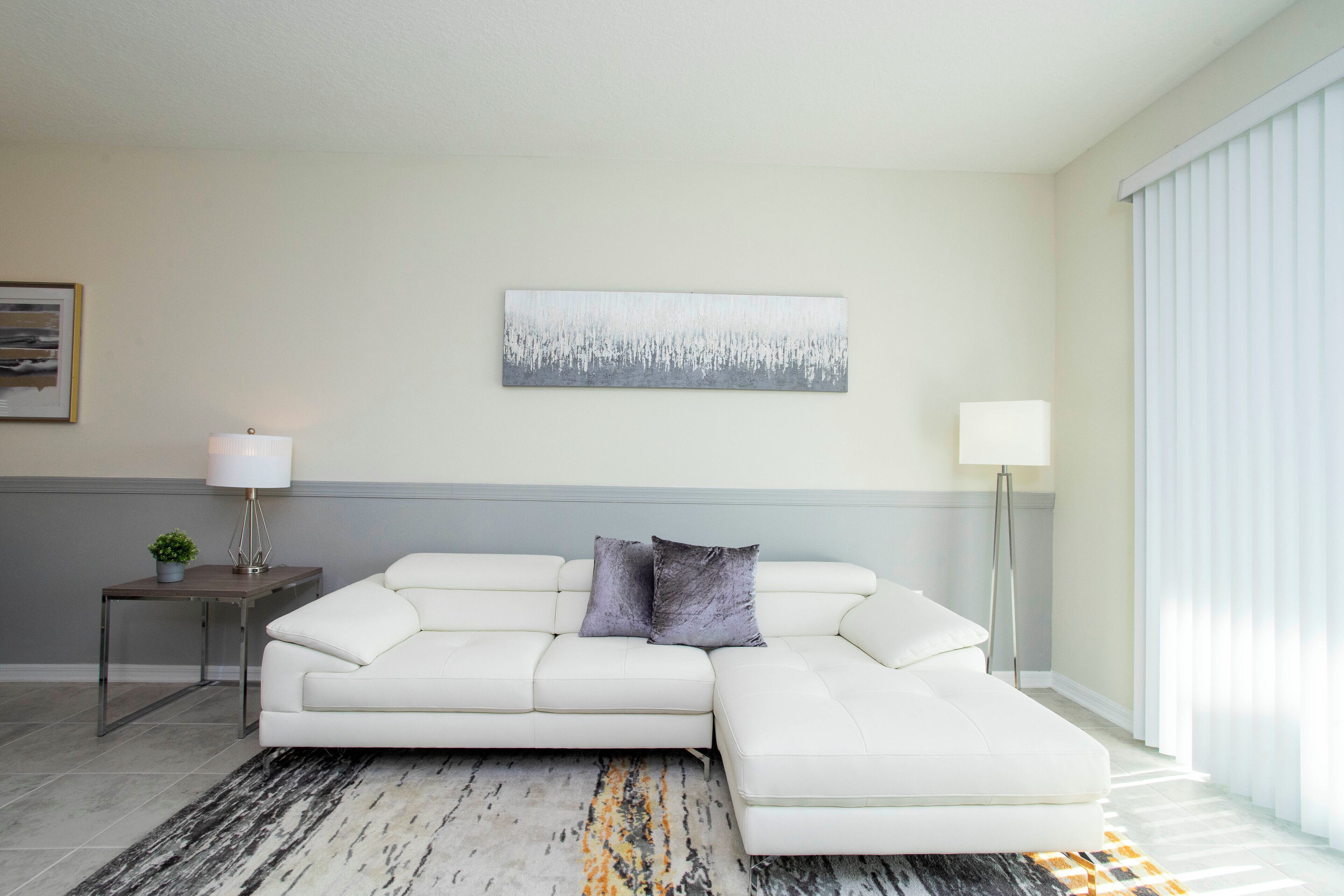 Uma sala de estar moderna com um sofá seccional branco, um tapete com padrão marmorizado e decoração minimalista.