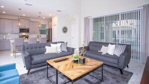 A modern living area with two sofas, a coffee table, and a kitchen in the background. - Gorgeous 5 Bd Home Close to Disney Storey Lake Resort 2734 (Kissimmee)