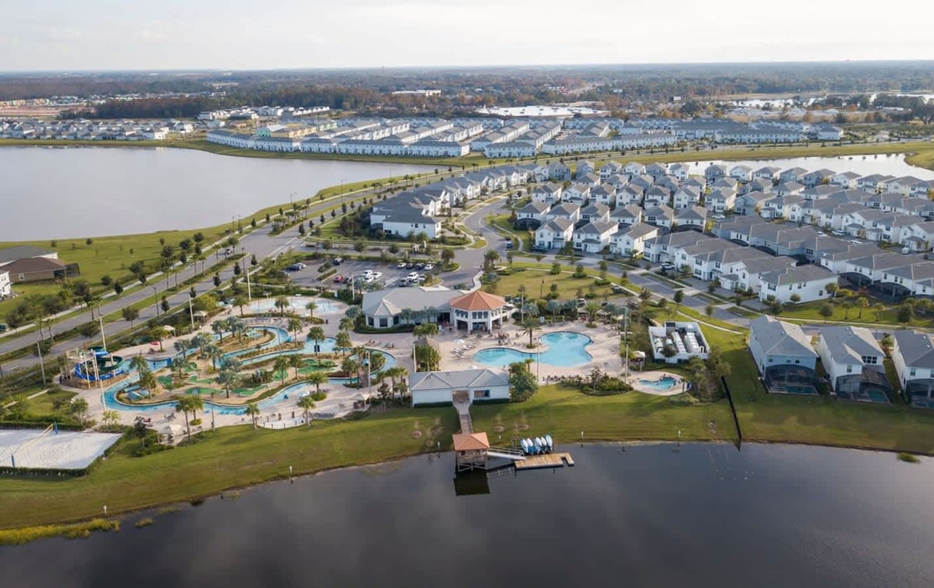 Vista aerea di una zona residenziale con un edificio centrale, un complesso di piscine e un lago.