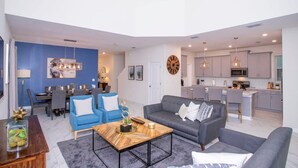 A modern living room with a sofa, coffee table, and dining area. - Gorgeous 5 Bd Home Close to Disney Storey Lake Resort 2734 (Kissimmee)