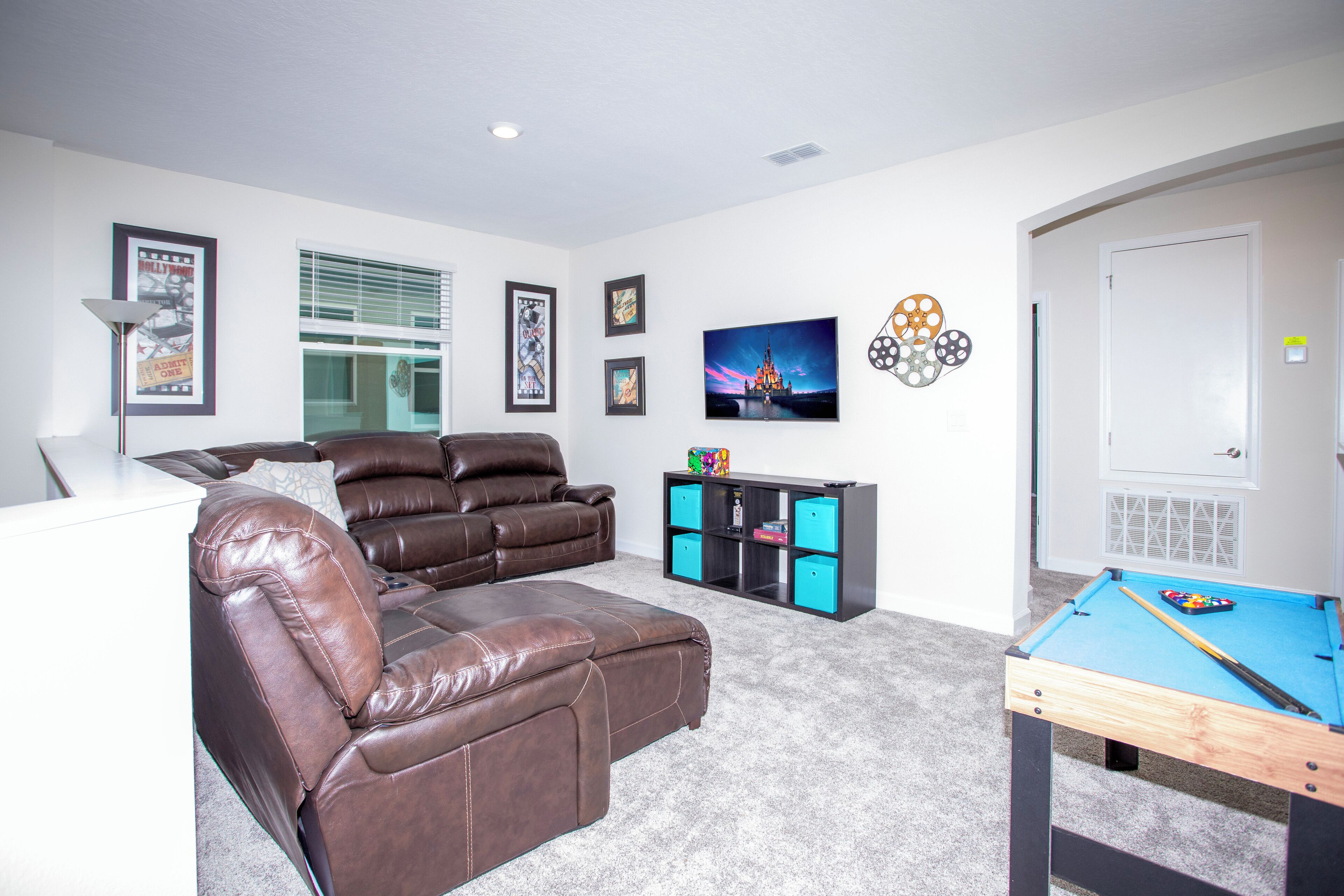 A living room with a brown leather sofa, a pool table, and a bookshelf.