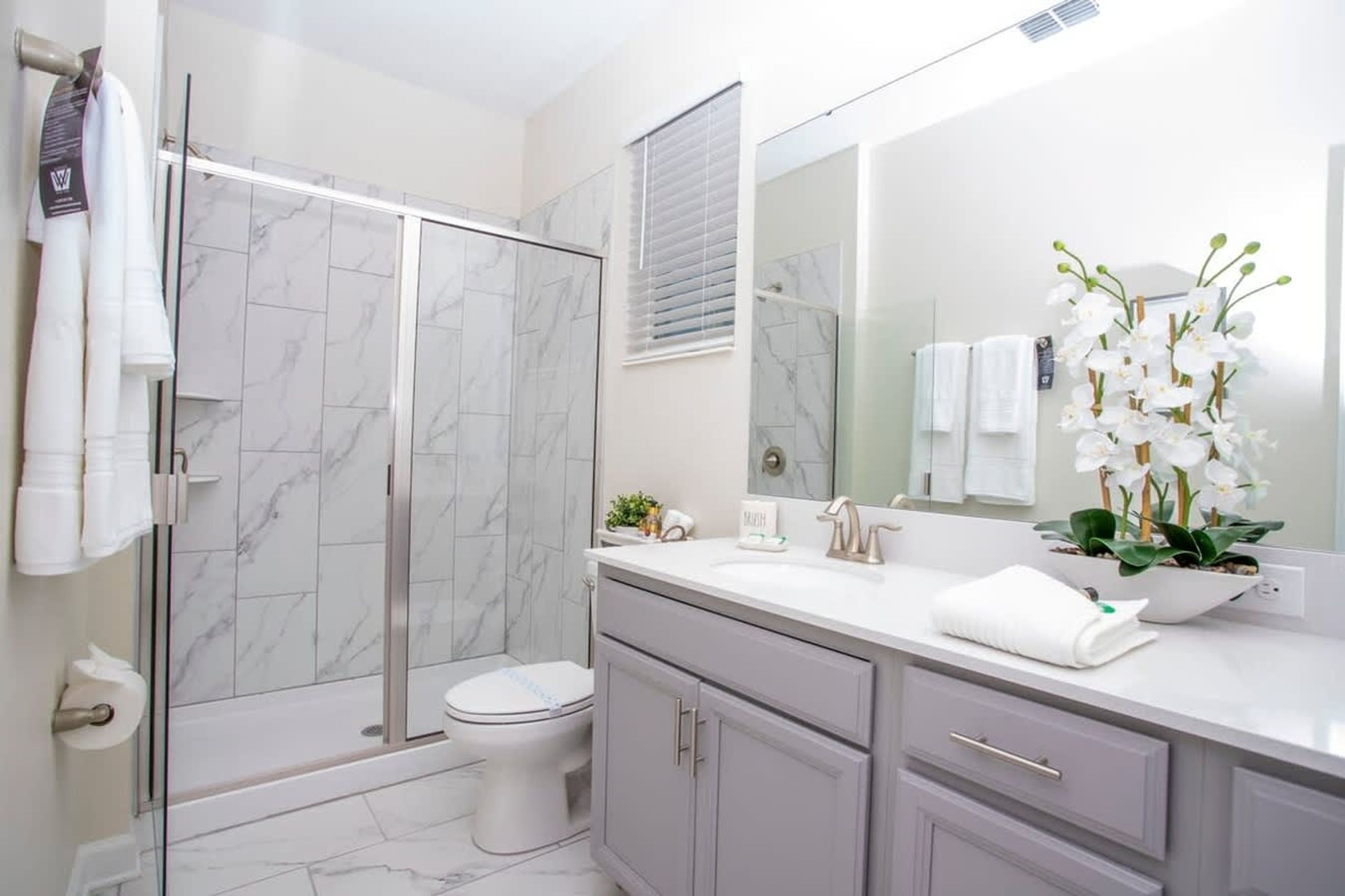 A bathroom with a glass-enclosed shower, a toilet, a sink with a mirror, and a potted orchid.