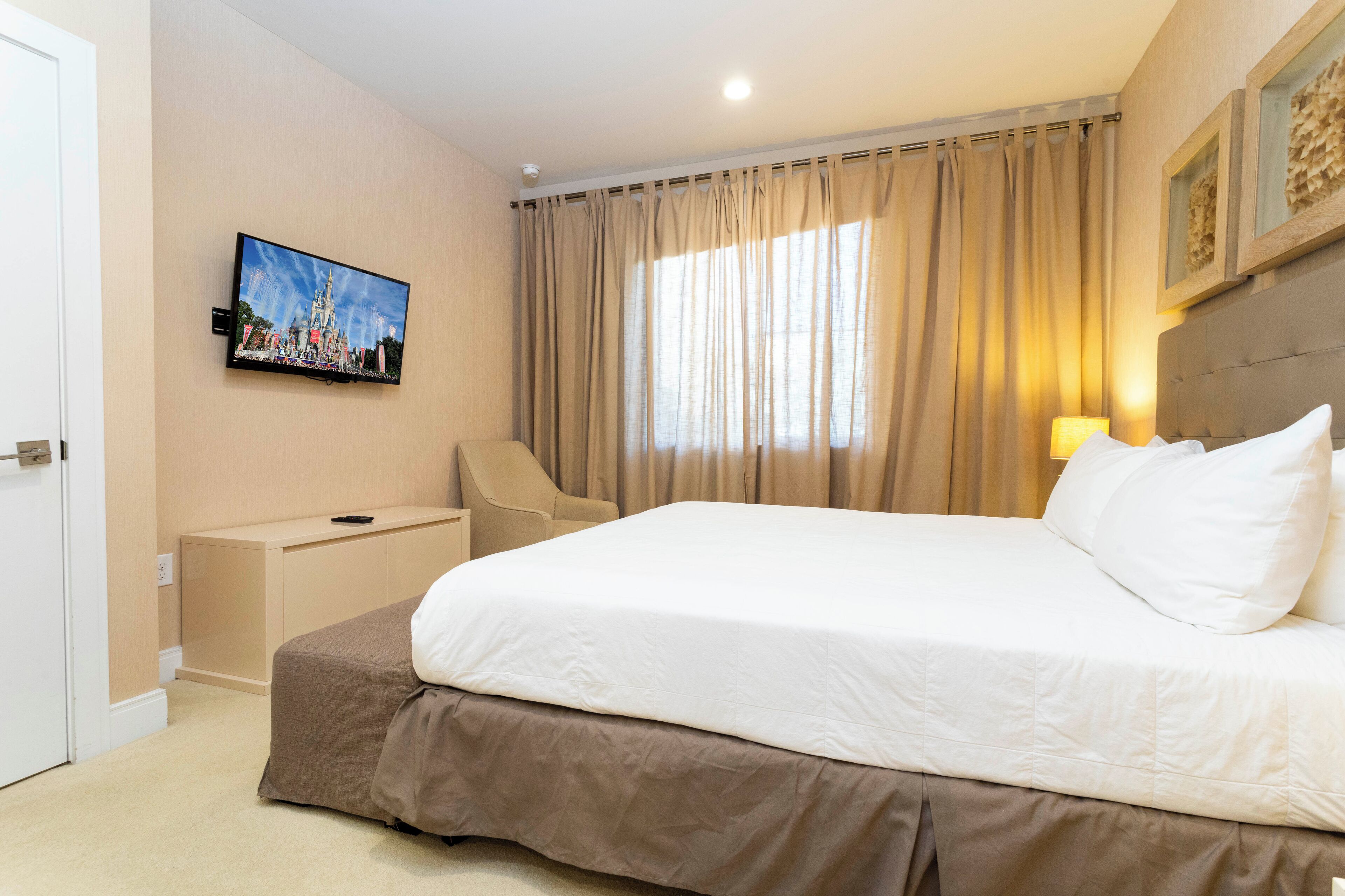A hotel room with a large bed, a television mounted on the wall, a chair, and a desk.