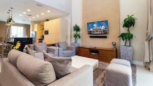 A modern living room with a sofa set, a flat-screen TV mounted on the wall, and a dining area in the background. - Gorgeous 4 Bd Close to Disney Magic Village 3114 (Kissimmee)