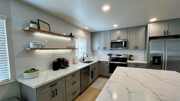 A modern kitchen with grey cabinets, a stainless steel refrigerator, a microwave, and a marble countertop. - Prime Location, Downtown Murphys (Murphys)